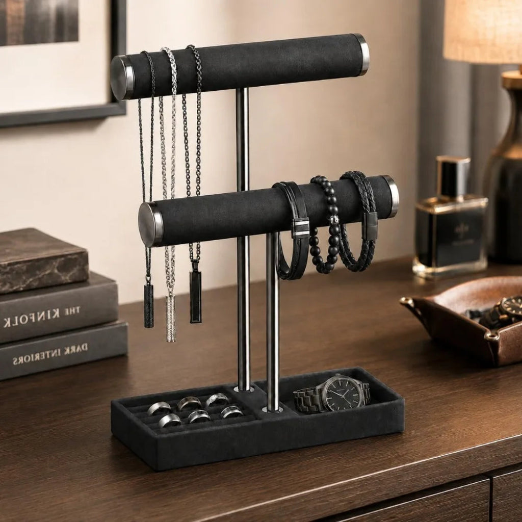 Black 2‑tier jewelry display stand on a dresser holding necklaces, bracelets, rings, and a watch in an organized velvet-lined base.