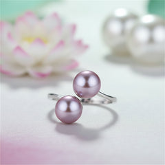 Sterling silver ring with double purple pearls with a white lotus flower and two iridescent white pearls blurred in the background.
