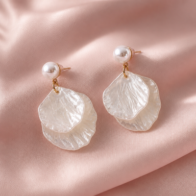 Mother‑of‑pearl double shell dangle earrings with white shell drops and gold‑tone metal accents on a pale pink background.