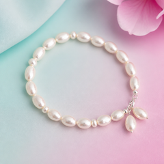 Close‑up white freshwater pearl bracelet with silver clasp and dangling pearls, displayed on a pastel aqua‑mint and lotus‑magenta background with soft lighting for a boutique product showcase.