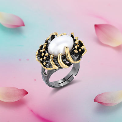 An artistic claw‑set silver ring featuring an 8×10mm natural baroque freshwater pearl, shown against a soft pastel pink‑blue‑purple background with scattered rose petals.