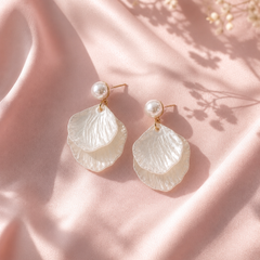 Pearl and petal-shaped earrings on a soft pink fabric background