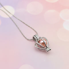 Silver heart‑shaped cage pendant holding a pink pearl on a delicate chain, displayed against a soft pastel background for an elegant, romantic jewelry presentation.