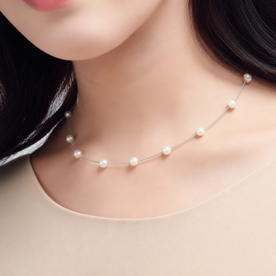 Sterling silver station necklace with evenly spaced micro‑pearls worn with a light neutral top.